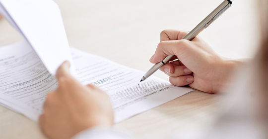 person with pen signing contract at desk